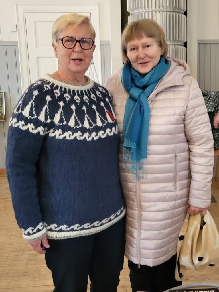 Kuvassa kaksi ihmistä, joista oikealla puolella olevalla päällään sininen villapaita.