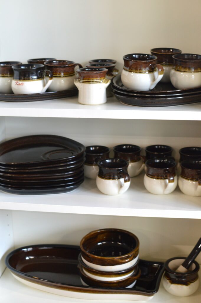 Kuva hyllystä, jossa on kolmella tasolla valko-ruskeita astioita.