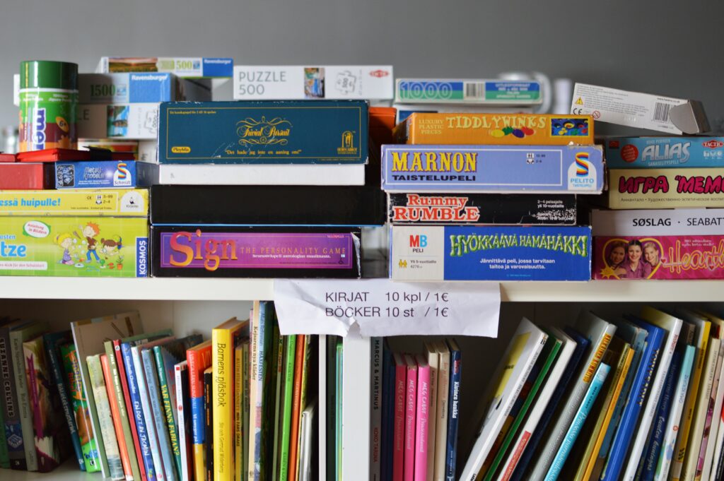 Kuva hyllystä, jossa on kirjoja ja lautapelejä. Hyllyyn on kiinnitetty lappu, jossa kymmenen kirjan yhteishinnaksi annetaan euro.